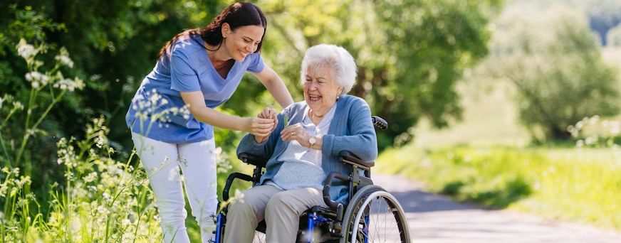 Life Assure Senior Woman Sitting In Chair And Laughing With Caregiver Nurse Hero